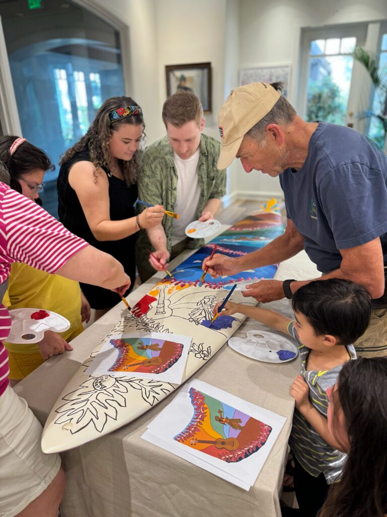 Guests contributing to a community surfboard art project during a live painting residency at the Ritz-Carlton in Maui.