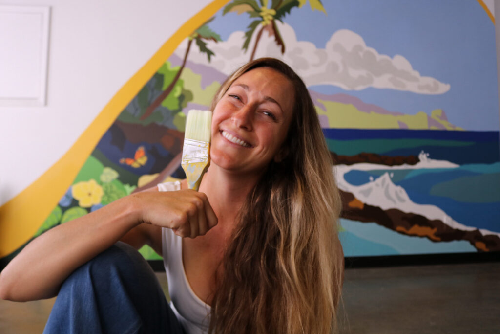 Maui mural artist in front of completed beach scene mural, open for new mural bookings.